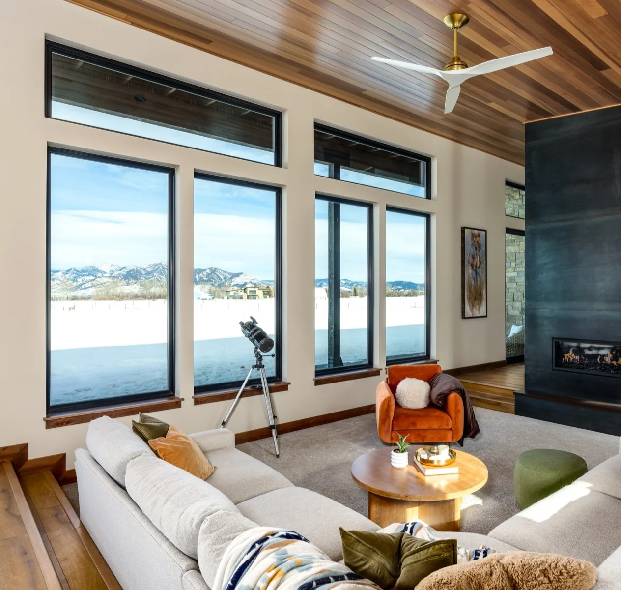 A living room with tall windows looking out at snow-covered mountains